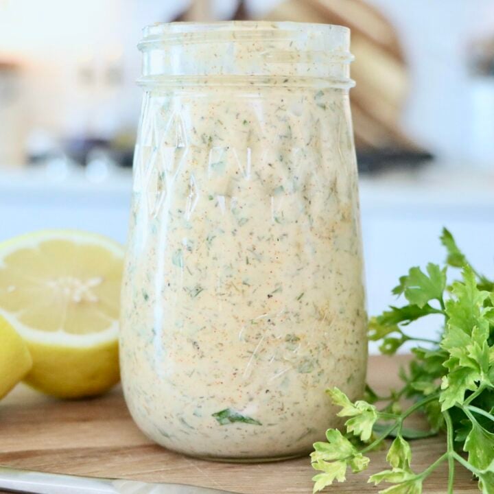 Herb Mayo in a glass jar on a cutting board next to a cut lemon and fresh parsley