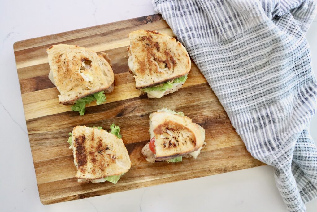 The ultimate chicken sandwich with sourdough bread and herb mayo on a cutting board with a towel next to it.