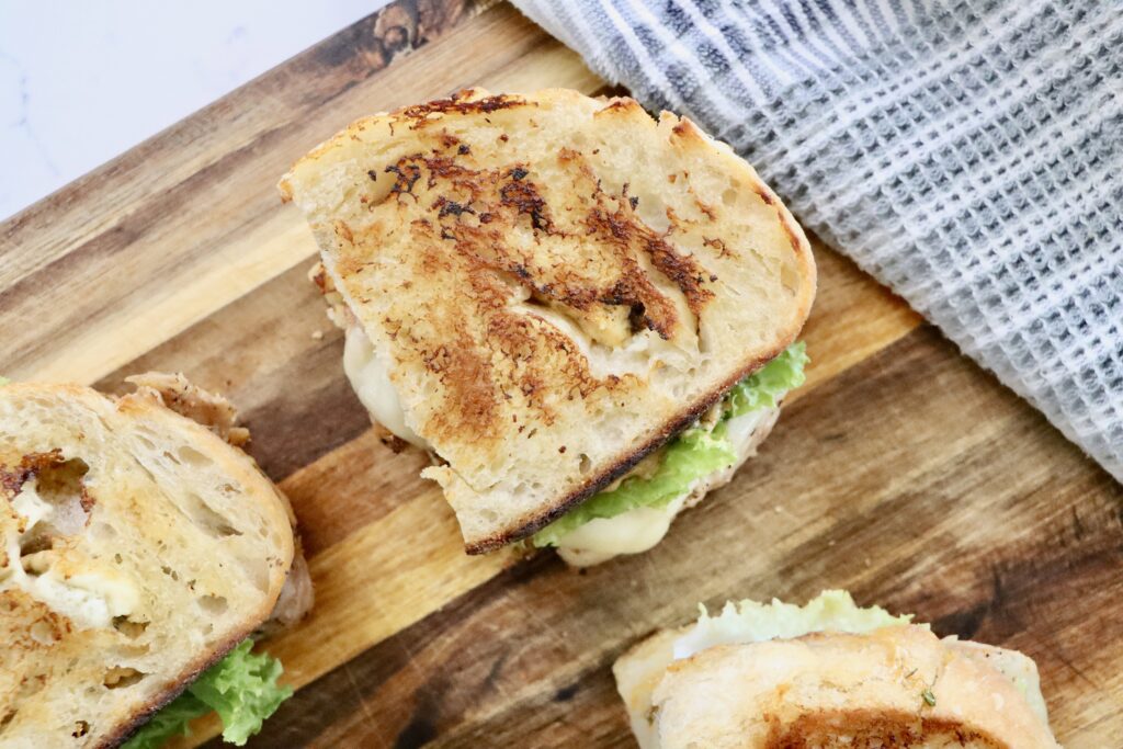 The ultimate chicken sandwich with sourdough bread and herb mayo on a cutting board with a towel next to it.