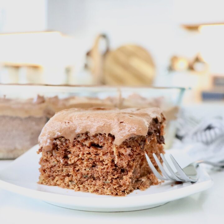 A slice of Moist Chocolate Zucchini Cake frosted with Chocolate Buttercream Frosting sitting on a white plate