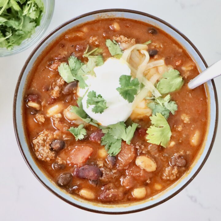 Hearty Homemade Chili in a bowl and pot next to bowls of cheese, cilantro and sour cream.