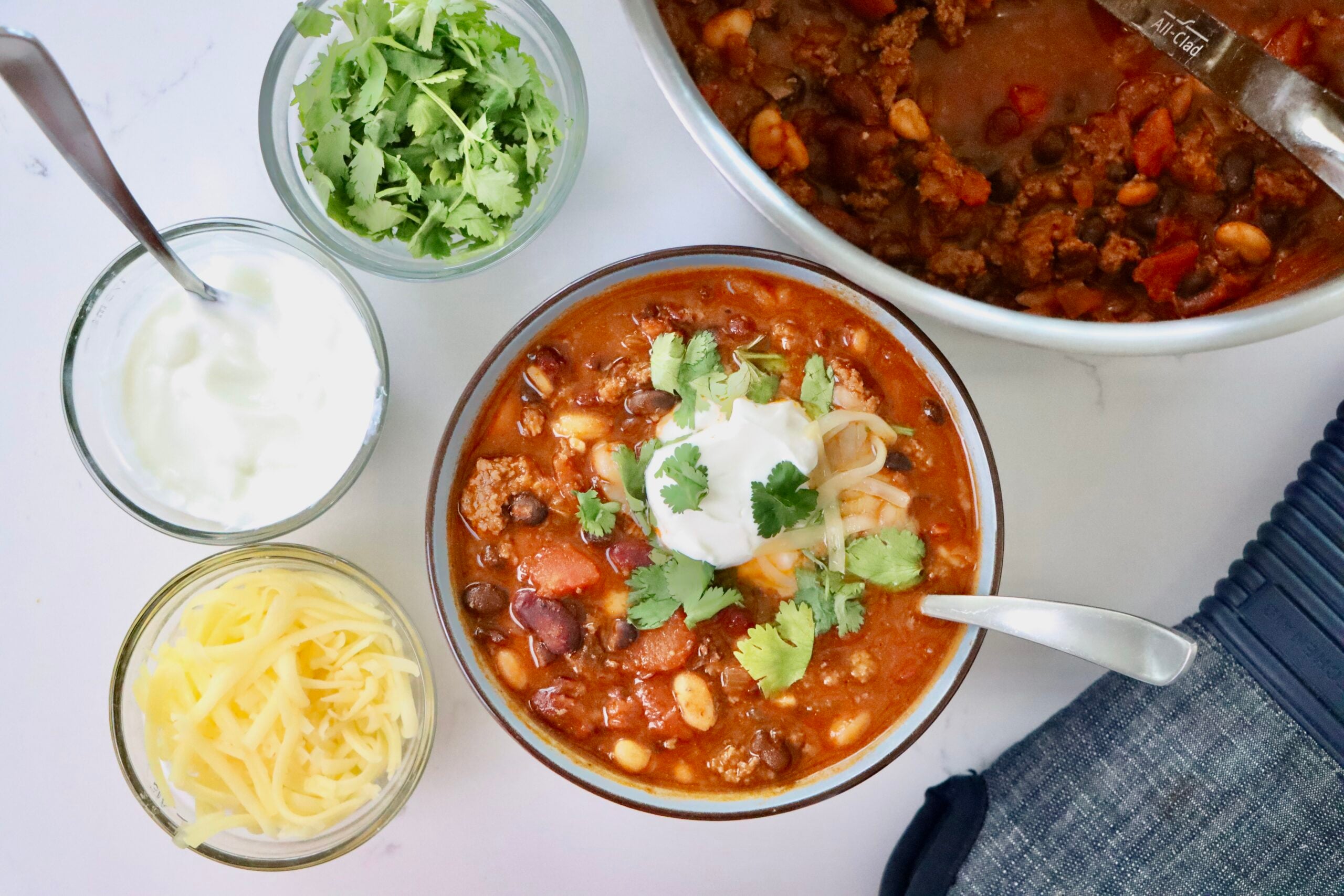 Hearty Homemade Chili in a bowl and pot next to bowls of cheese, cilantro and sour cream.