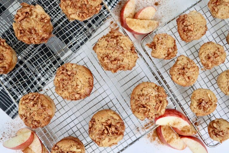 Soft and moist homemade apple muffins topped with diced apples and turbinado sugar on a cooling rack, made from scratch with applesauce and Greek yogurt.