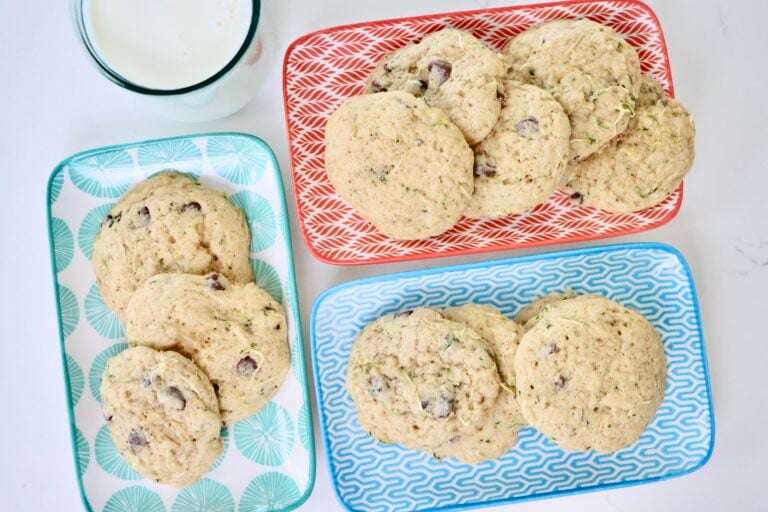 Trays of soft and chewy chocolate chip zucchini cookies, baked from scratch with real ingredients, including grated zucchini, organic sugars, and melty semi-sweet chocolate chips. The cookies are golden brown, slightly crisp on the edges, and perfectly moist in the center.