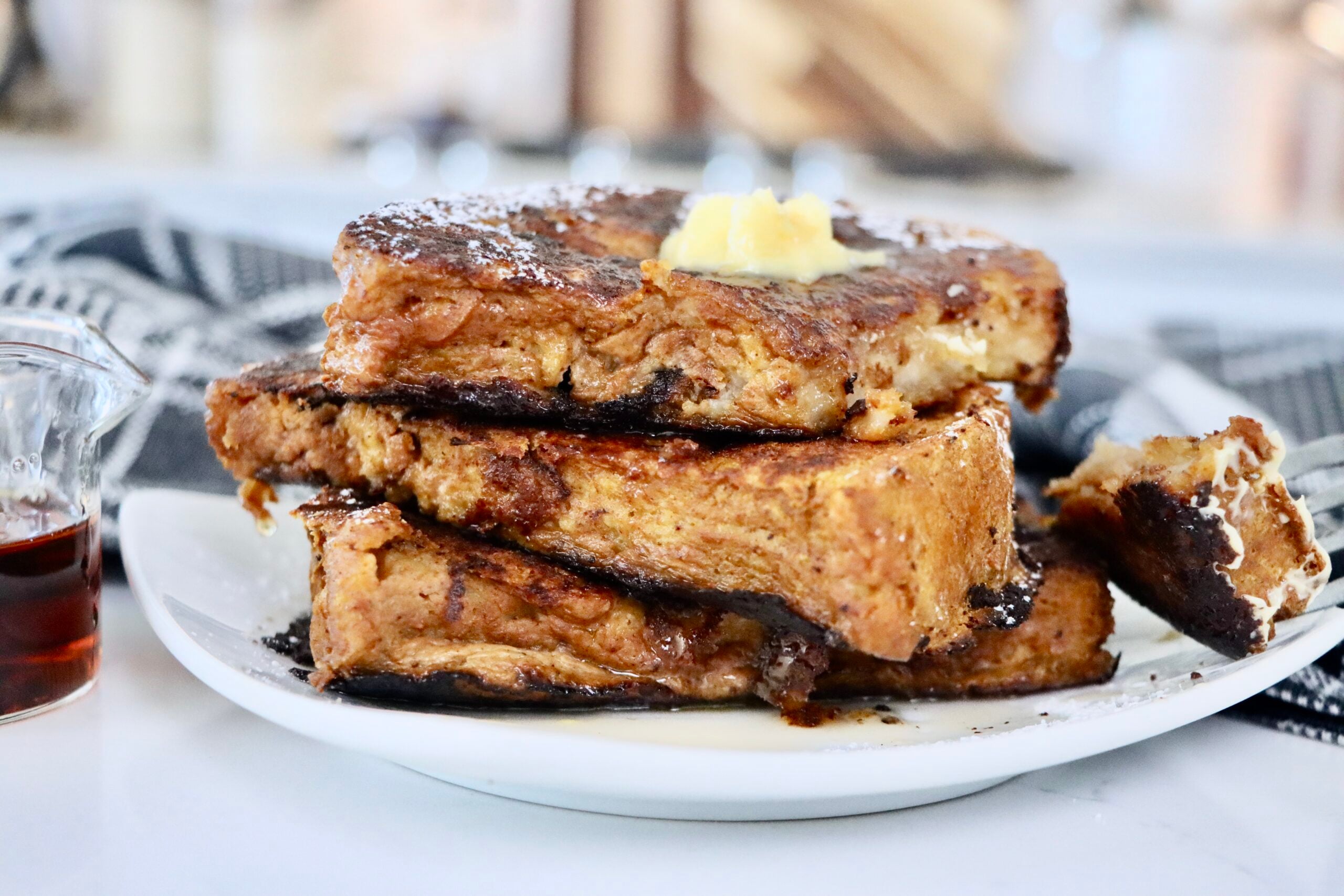 A stack of golden-brown pumpkin French toast made with thick slices of sourdough bread, topped with maple syrup, a and a sprinkle of powdered sugar.
