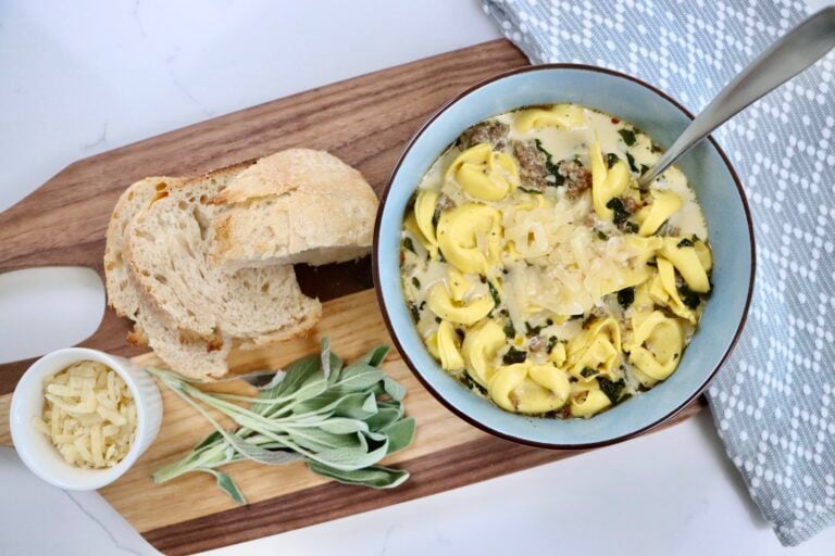 Bowl of homemade creamy sausage tortellini soup served with crusty bread on the side, ready for a cozy dinner.