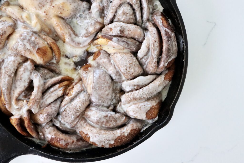 Golden braided sourdough cinnamon wreath baked to perfection in a cast iron skillet with layers of cinnamon sugar and drizzled frosting.