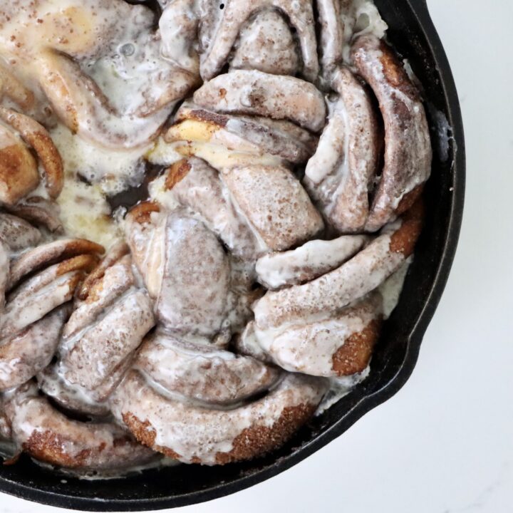 Golden braided sourdough cinnamon wreath baked to perfection in a cast iron skillet with layers of cinnamon sugar and drizzled frosting.