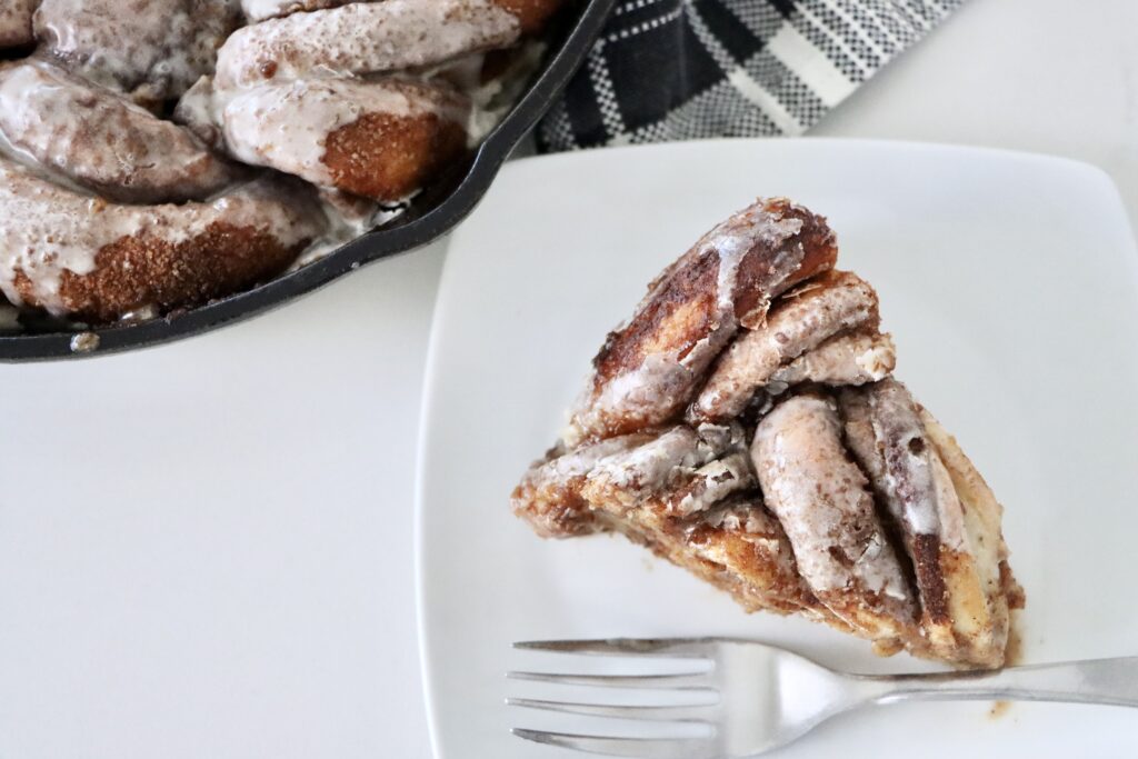 Golden braided sourdough cinnamon wreath baked to perfection in a cast iron skillet with layers of cinnamon sugar and drizzled frosting.