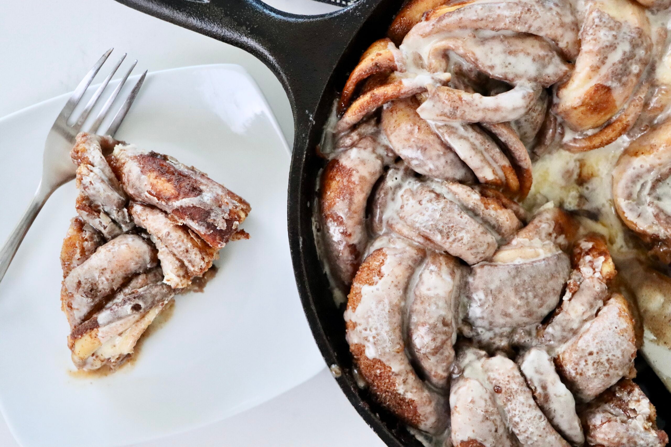 Golden braided sourdough cinnamon wreath baked to perfection in a cast iron skillet with layers of cinnamon sugar and drizzled frosting.