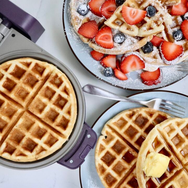 Golden, crispy sourdough waffles stacked on a plate with fresh berries and maple syrup, made from scratch with whole ingredients and an easy overnight ferment.
