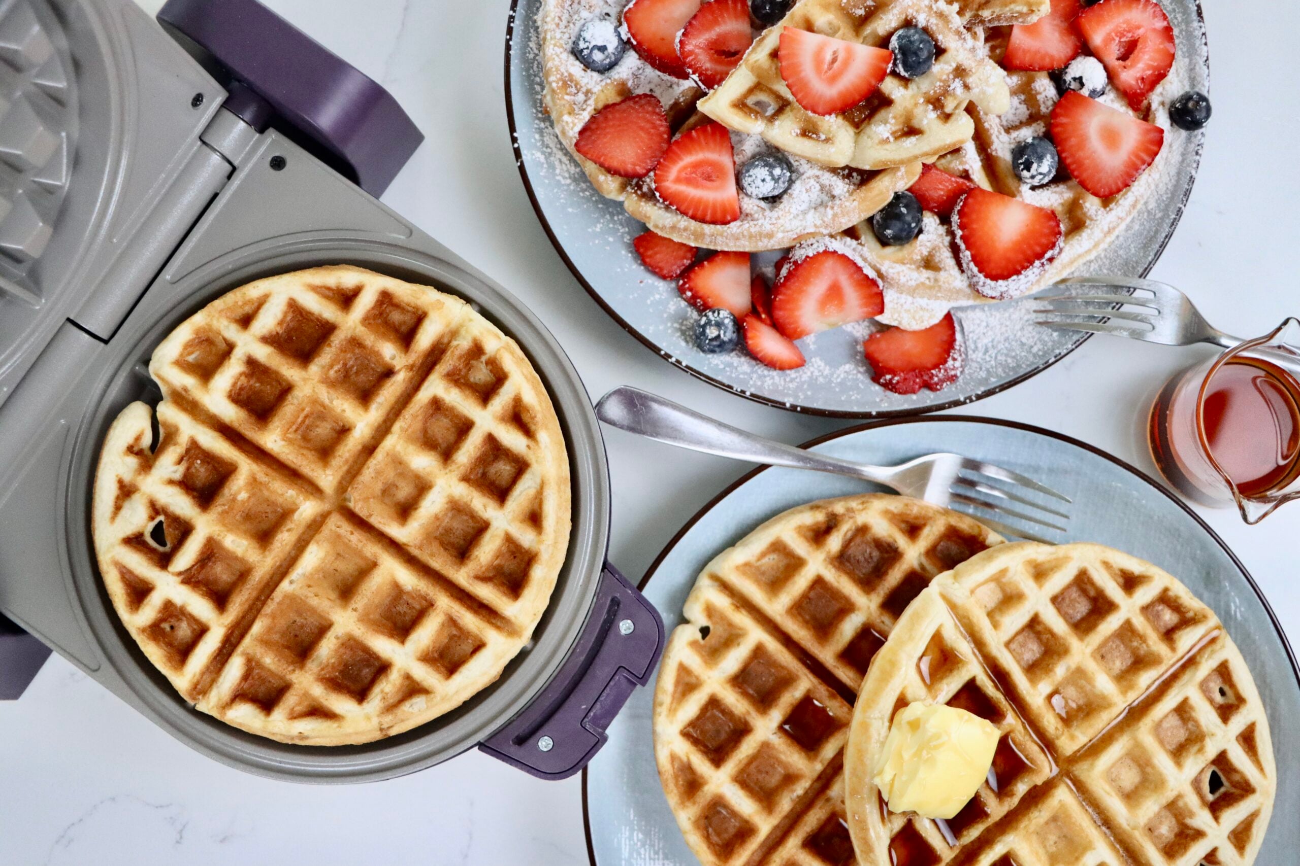 Golden, crispy sourdough waffles stacked on a plate with fresh berries and maple syrup, made from scratch with whole ingredients and an easy overnight ferment.