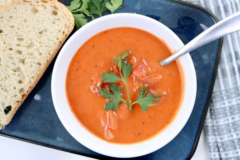 A bowl of creamy homemade tomato soup made from scratch with real ingredients—fresh tomatoes, milk, and butter—garnished with parsley and served with crusty bread.