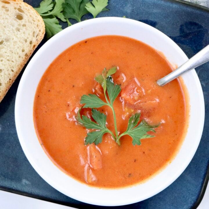 A bowl of creamy homemade tomato soup made from scratch with real ingredients—fresh tomatoes, milk, and butter—garnished with parsley and served with crusty bread.