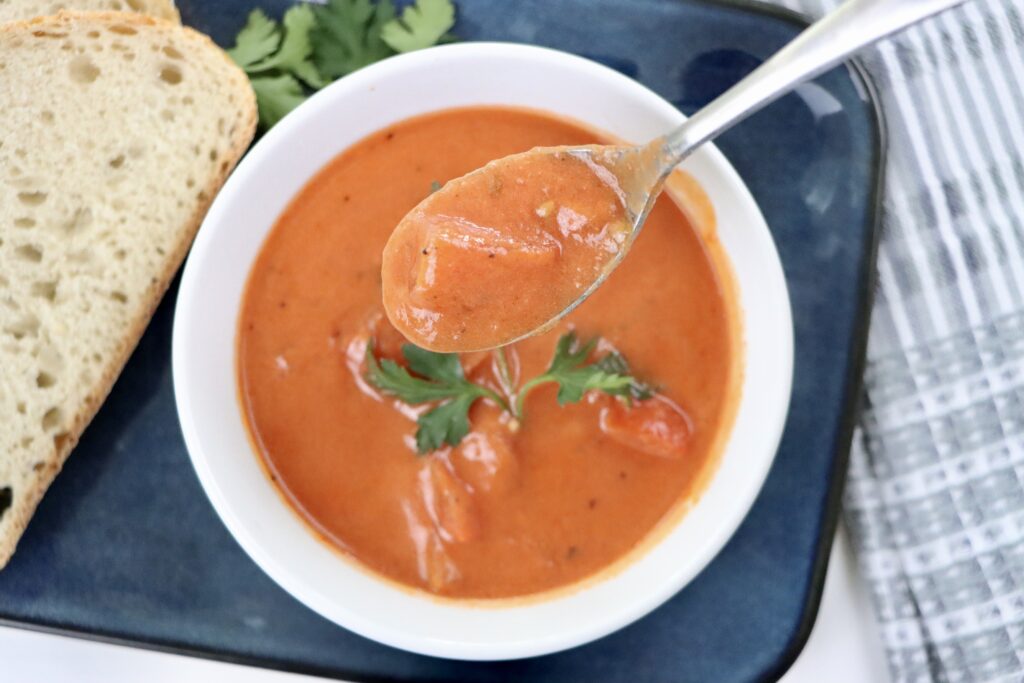 A bowl of creamy homemade tomato soup made from scratch with real ingredients—fresh tomatoes, milk, and butter—garnished with parsley and served with crusty bread.