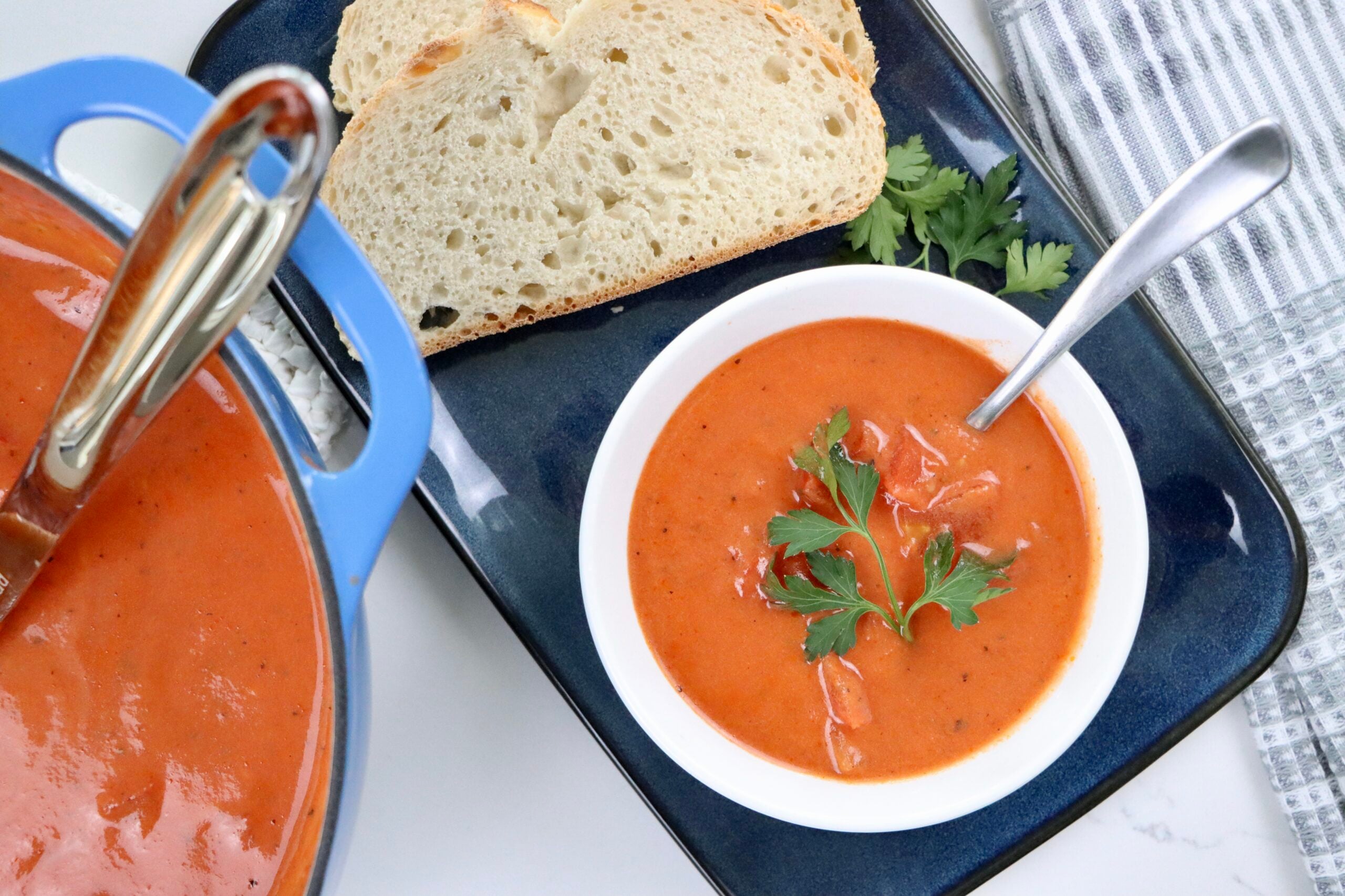 A bowl of creamy homemade tomato soup made from scratch with real ingredients—fresh tomatoes, milk, and butter—garnished with parsley and served with crusty bread.