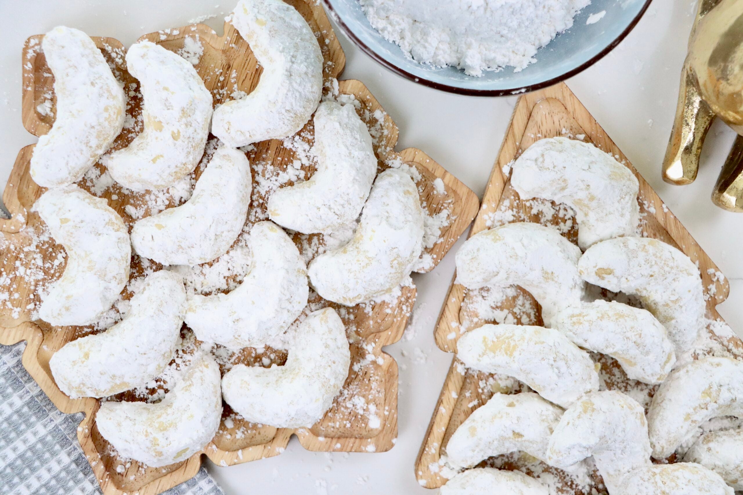 Freshly baked Kifflings (Almond Crescent Cookies) dusted with powdered sugar on a Christmas tray.