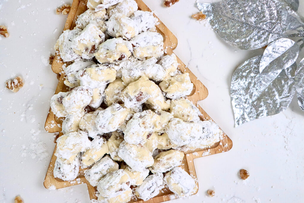 Close-up of stuffed dates with walnuts and cream cheese frosting rolled in powdered sugar on a holiday serving tray.