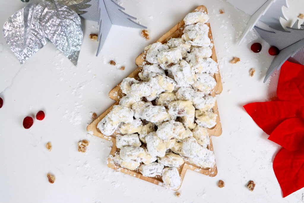 Close-up of stuffed dates with walnuts and cream cheese frosting rolled in powdered sugar on a holiday serving tray.