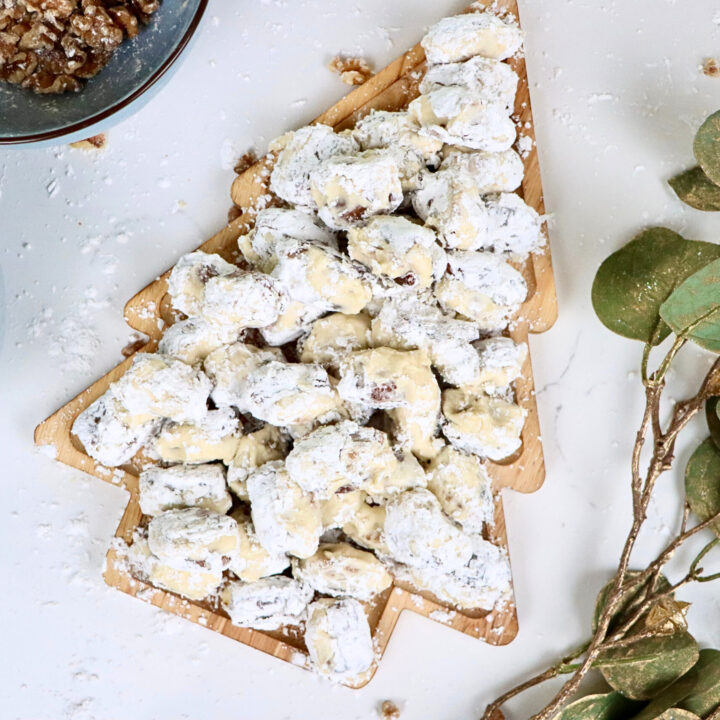 Close-up of stuffed dates with walnuts and cream cheese frosting rolled in powdered sugar on a holiday serving tray.