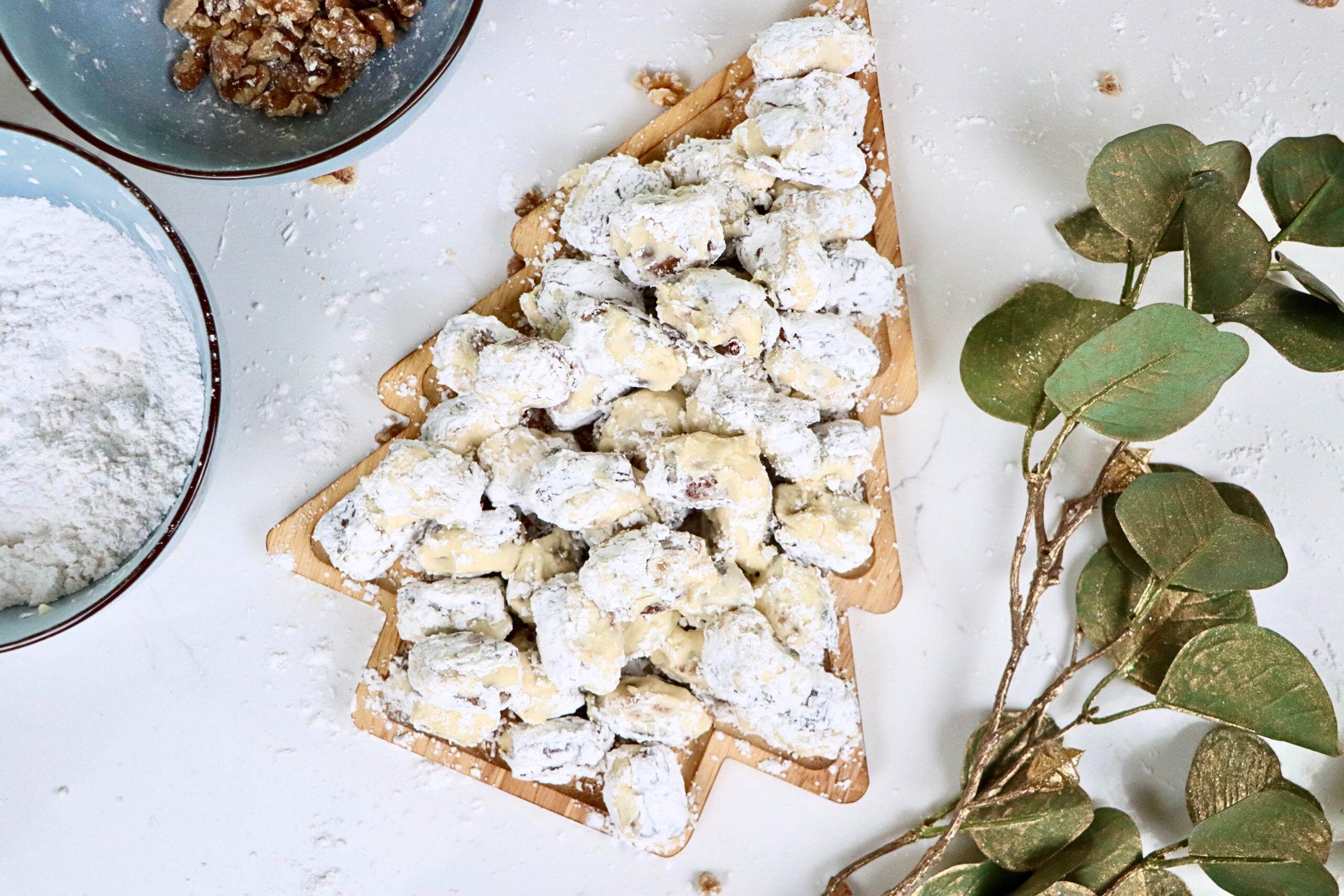 Close-up of stuffed dates with walnuts and cream cheese frosting rolled in powdered sugar on a holiday serving tray.