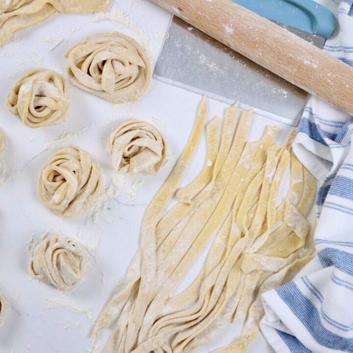 Fresh pasta being cut into fettuccine noodles by hand on a floured countertop, from scratch at home.