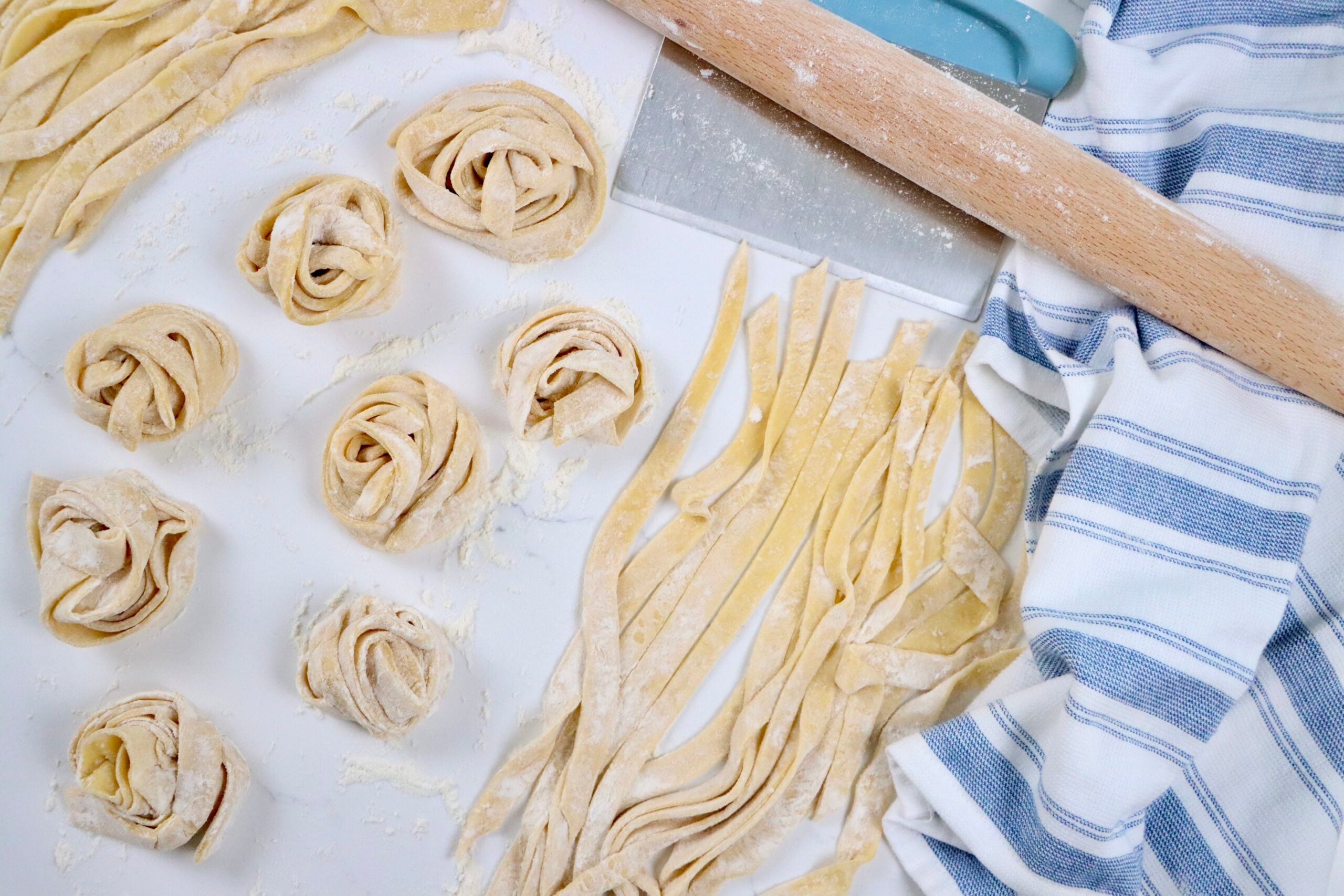 Fresh pasta being cut into fettuccine noodles by hand on a floured countertop, from scratch at home.