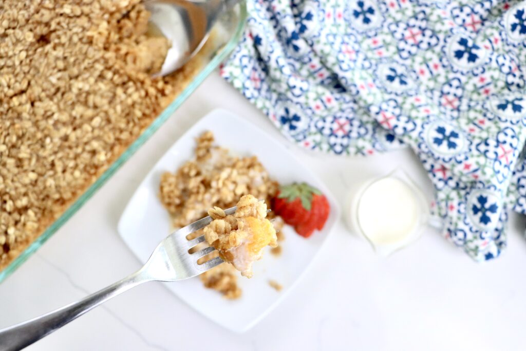 Baked oatmeal with fresh peaches in a 9x13 pan and a white plate, golden and fluffy, drizzled with cream, ready to serve for breakfast