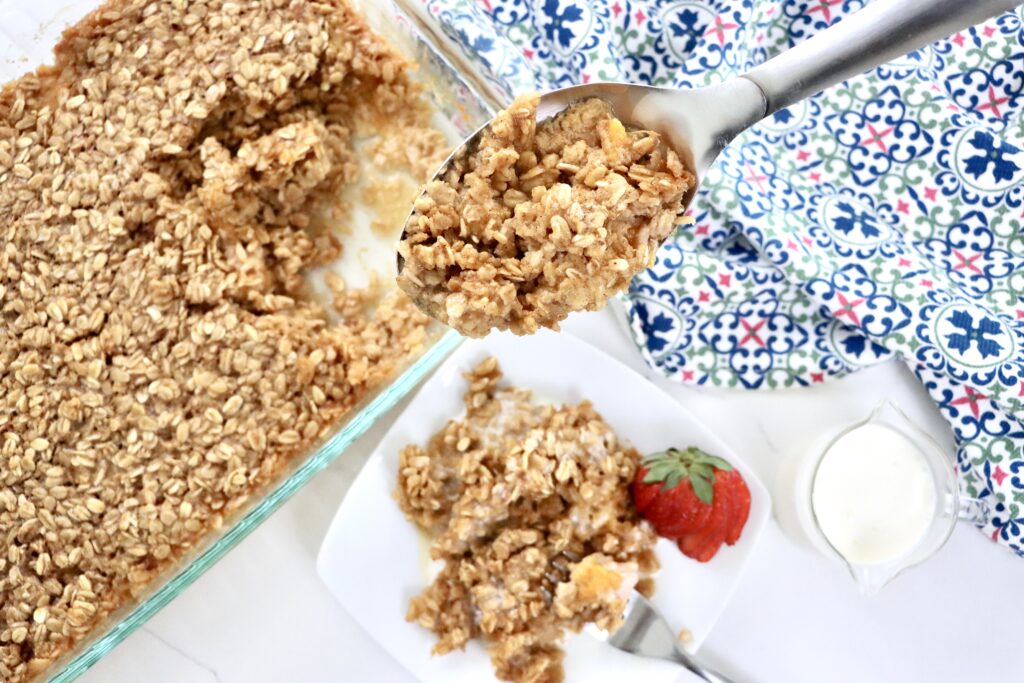 Baked oatmeal with fresh peaches in a 9x13 pan and a white plate, golden and fluffy, drizzled with cream, ready to serve for breakfast