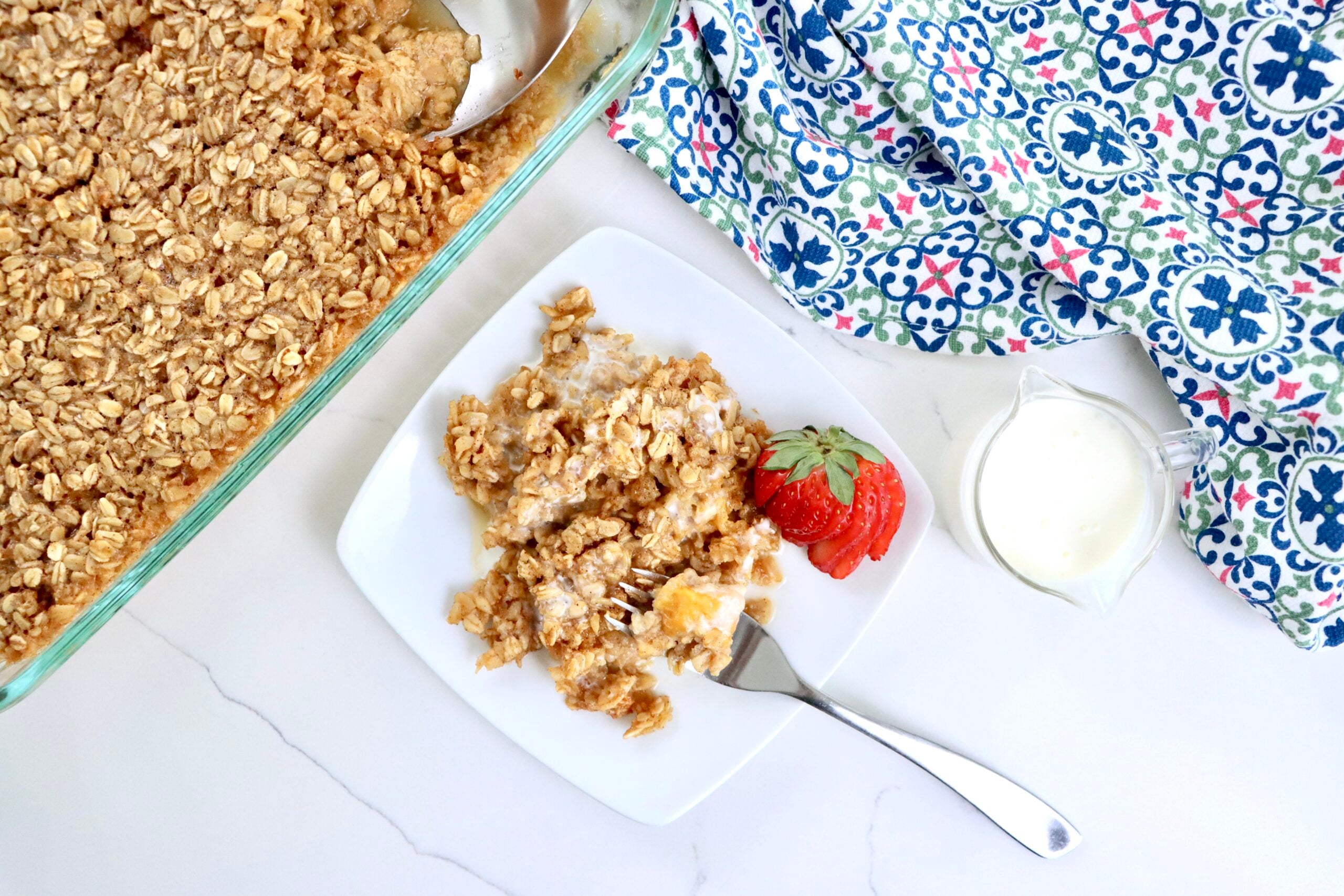 Baked oatmeal with fresh peaches in a 9x13 pan and a white plate, golden and fluffy, drizzled with cream, ready to serve for breakfast