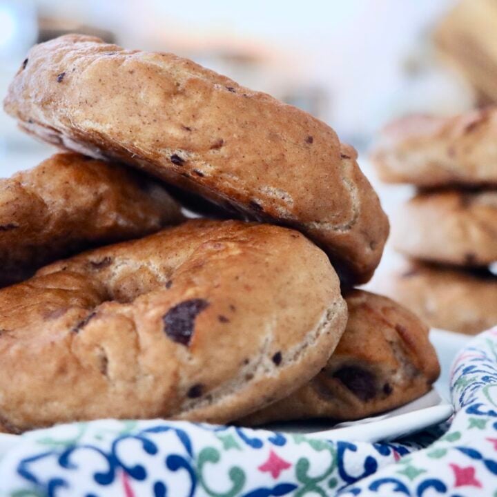 Stack of homemade sourdough cinnamon raisin bagels with a glossy bakery-style crust on a kitchen counter.