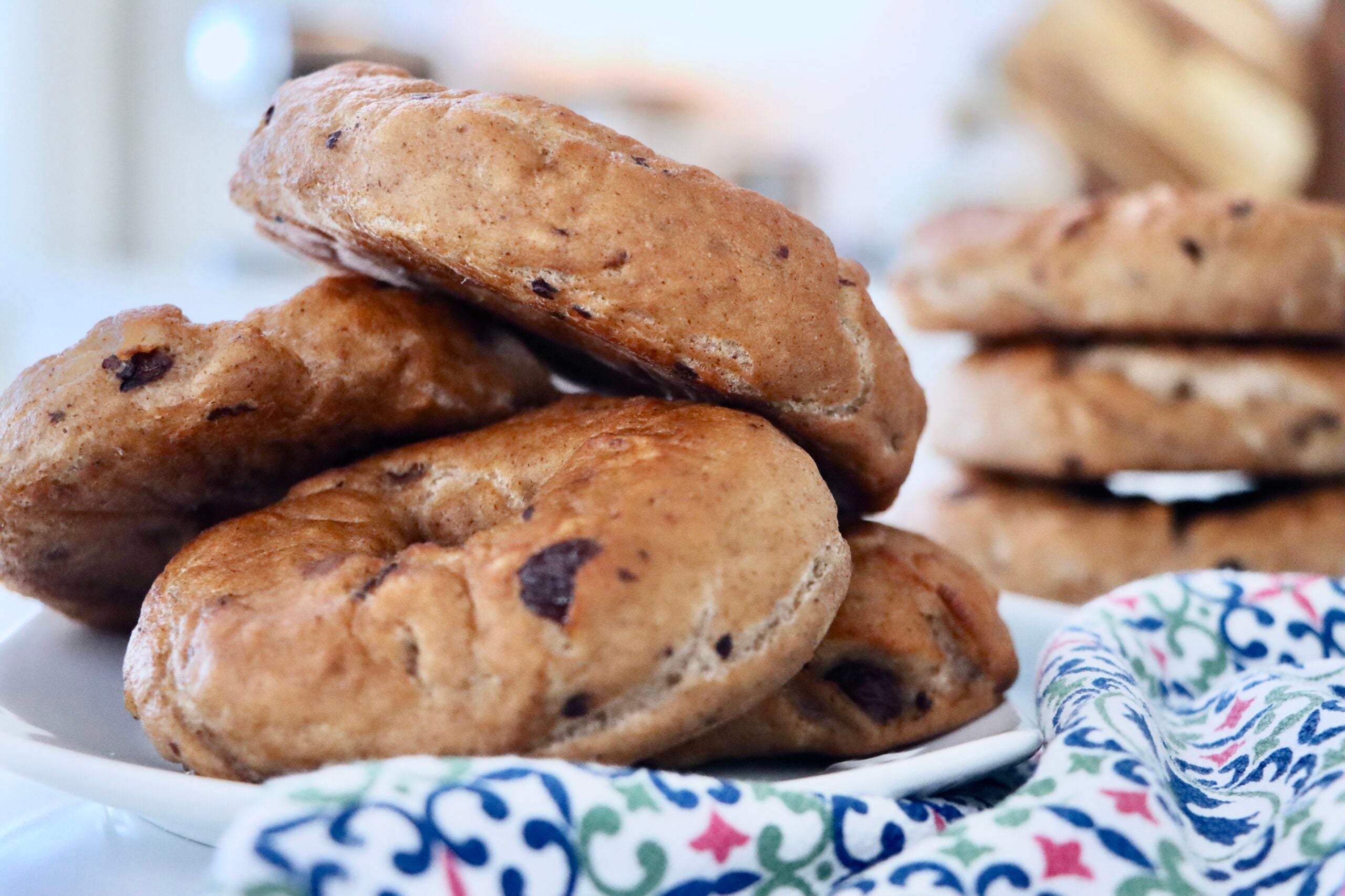 Stack of homemade sourdough cinnamon raisin bagels with a glossy bakery-style crust on a kitchen counter.