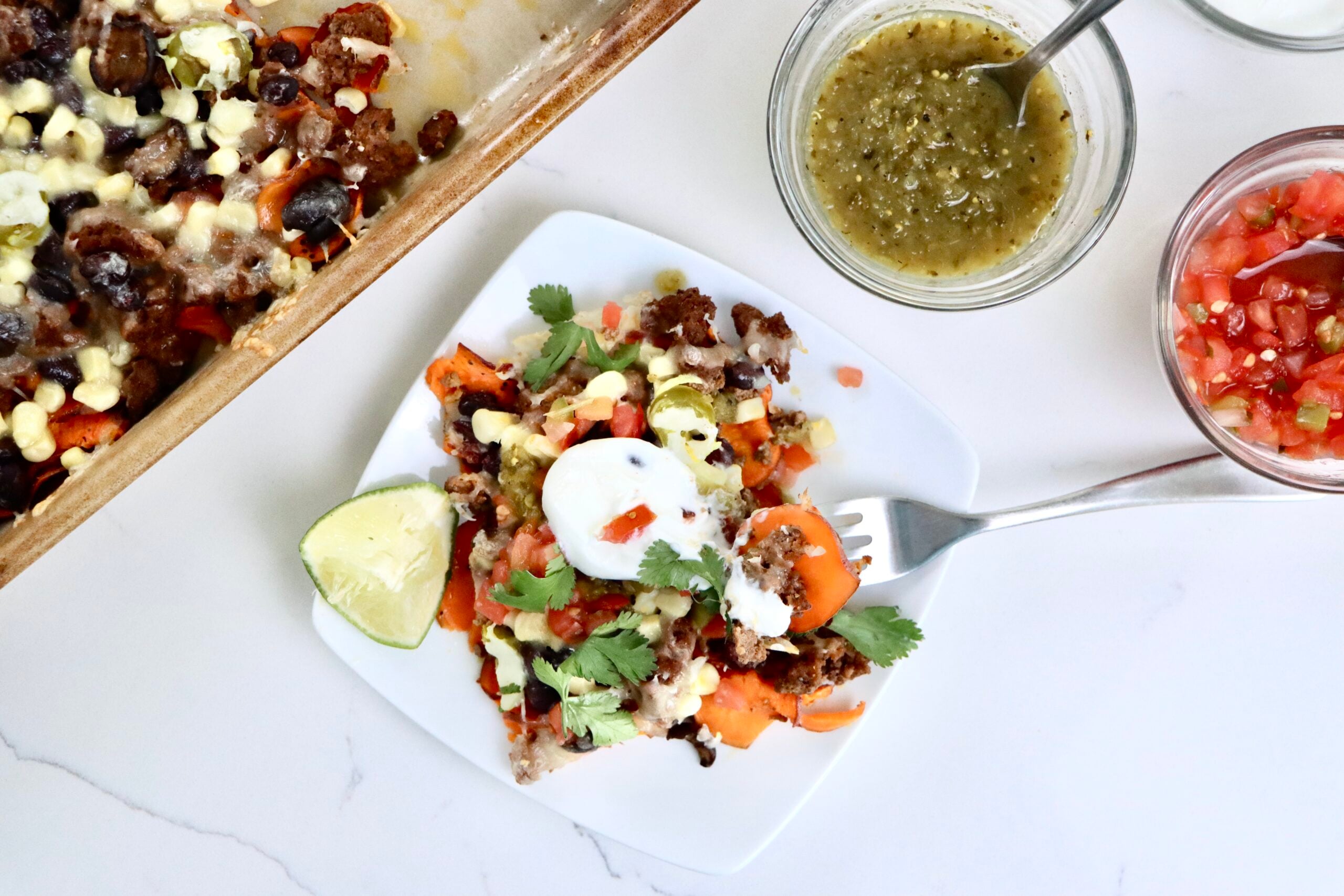 Sheet pan sweet potato nachos with melted cheddar, seasoned ground beef, black beans, corn, and fresh toppings