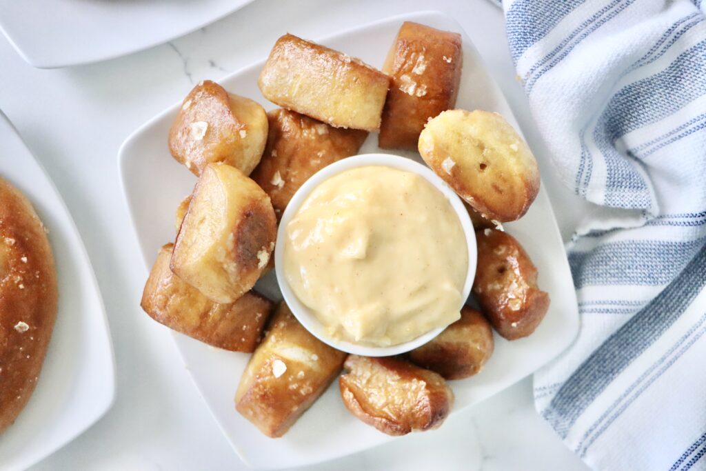 Close-up of creamy homemade cheddar cheese sauce in a small bowl with soft pretzels ready for dipping.
