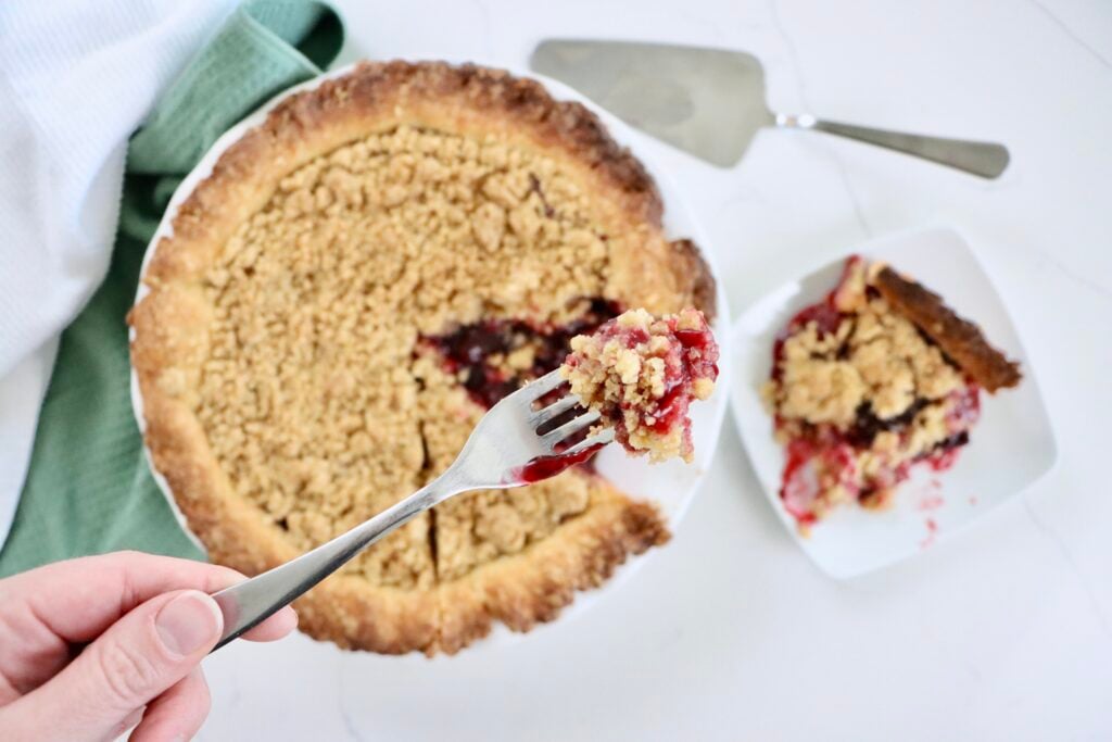 Golden Dutch Cherry Pie with buttery crumb topping, thick homemade cherry filling bubbling through, served in a white pie dish.