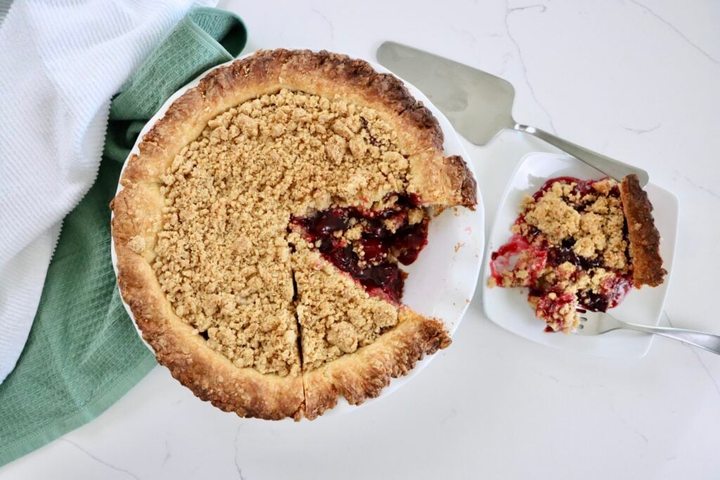 Golden Dutch Cherry Pie with buttery crumb topping, thick homemade cherry filling bubbling through, served in a white pie dish.