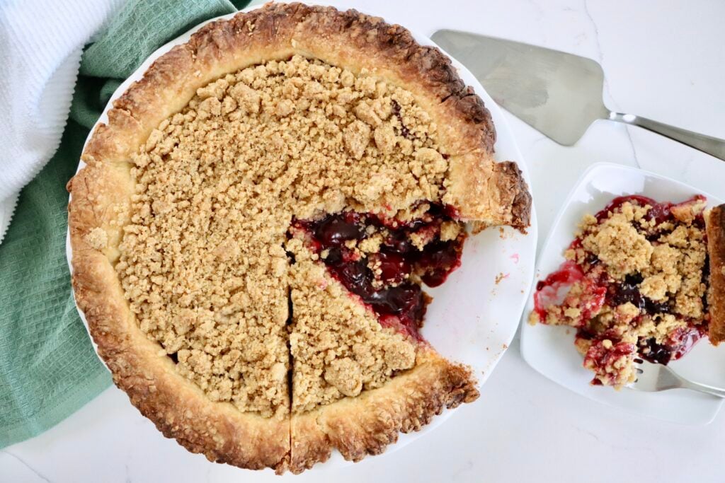 Golden Dutch Cherry Pie with buttery crumb topping, thick homemade cherry filling bubbling through, served in a white pie dish.