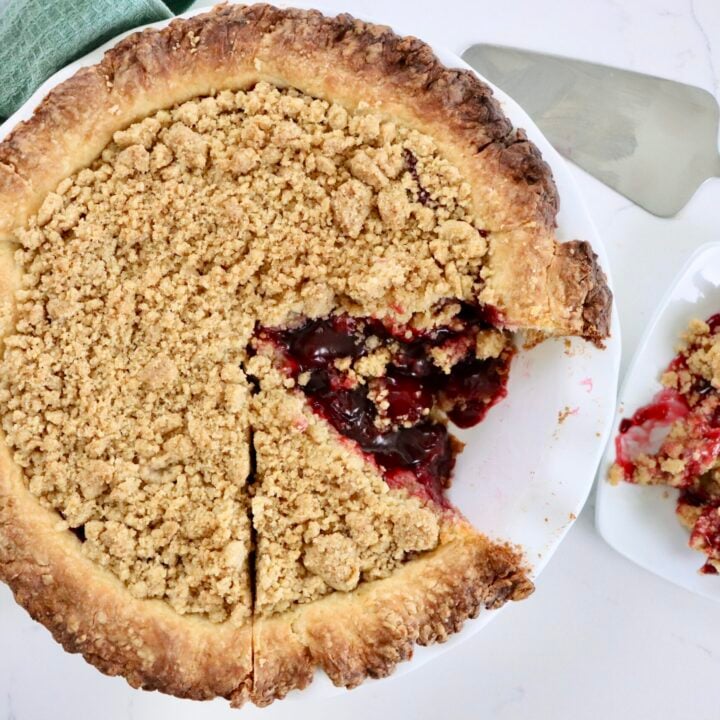 Golden Dutch Cherry Pie with buttery crumb topping, thick homemade cherry filling bubbling through, served in a white pie dish.