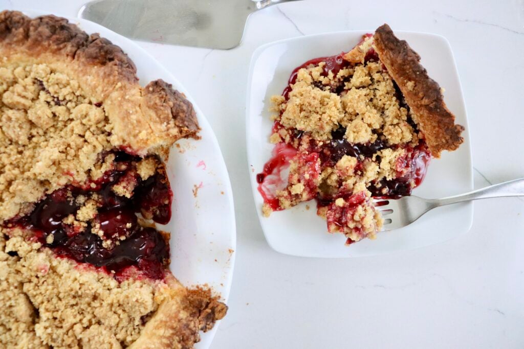 Golden Dutch Cherry Pie with buttery crumb topping, thick homemade cherry filling bubbling through, served in a white pie dish.