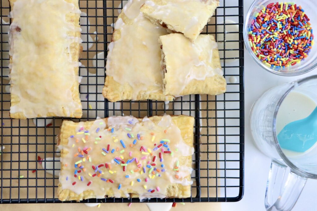 Flaky homemade pop tarts on cooling rack, filled with berry jam, drizzled with glaze, made from scratch with real ingredients.