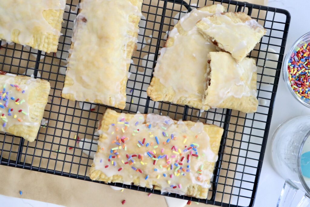 Flaky homemade pop tarts on cooling rack, filled with berry jam, drizzled with glaze, made from scratch with real ingredients.