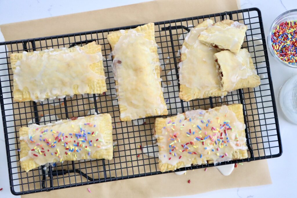 Flaky homemade pop tarts on cooling rack, filled with berry jam, drizzled with glaze, made from scratch with real ingredients.