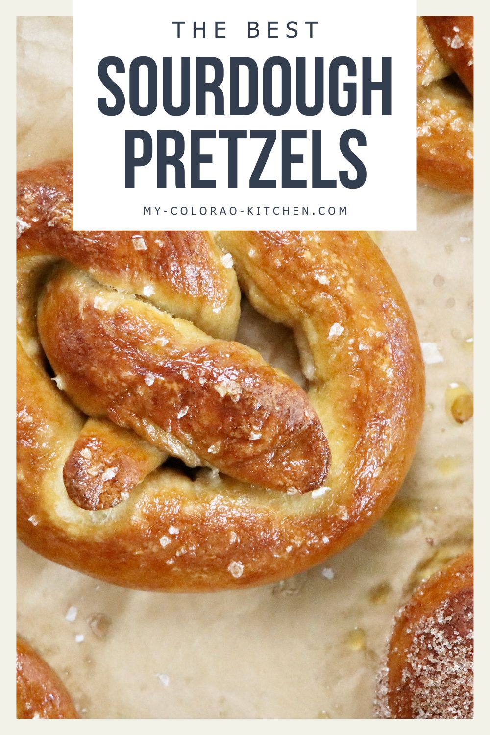 Soft, golden brown sourdough pretzels fresh out of the oven, sprinkled with Maldon salt on a parchment-lined baking sheet, homemade from scratch.