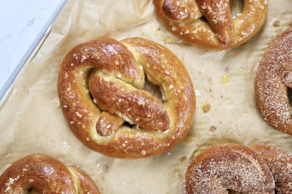 Soft, golden brown sourdough pretzels fresh out of the oven, sprinkled with Maldon salt on a parchment-lined baking sheet, homemade from scratch.