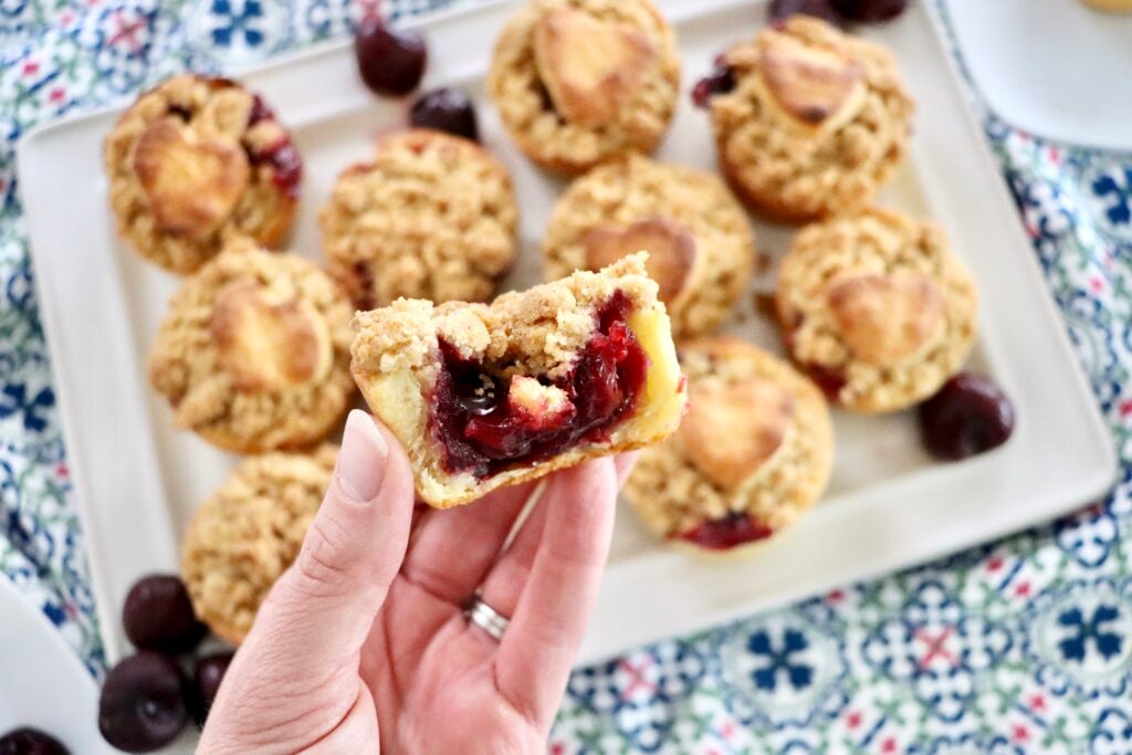 Handheld mini cherry pies with buttery streusel topping, fresh cherries bubbling inside.