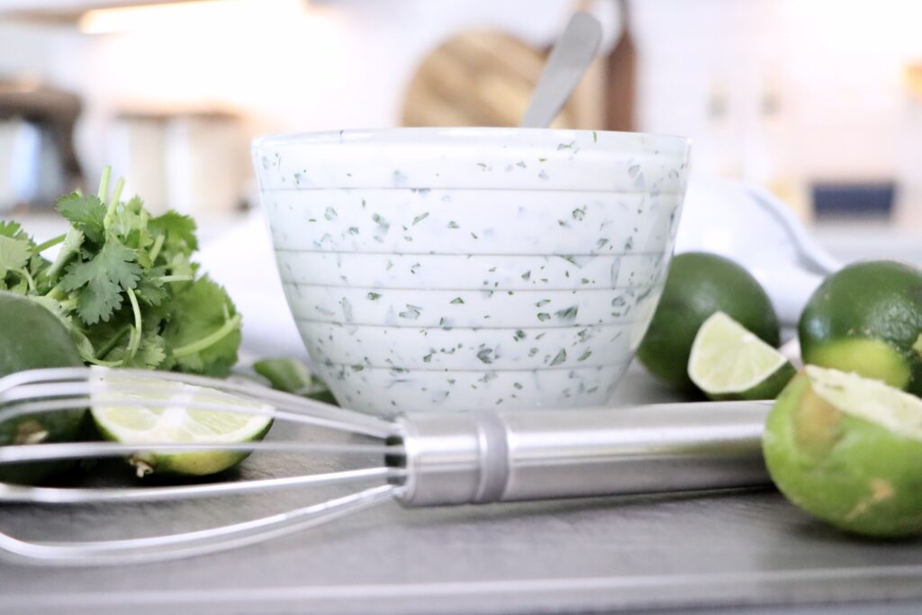 Fresh cilantro lime crema in a white bowl, vibrant green flecks of cilantro visible, perfect easy 5-minute taco sauce recipe.