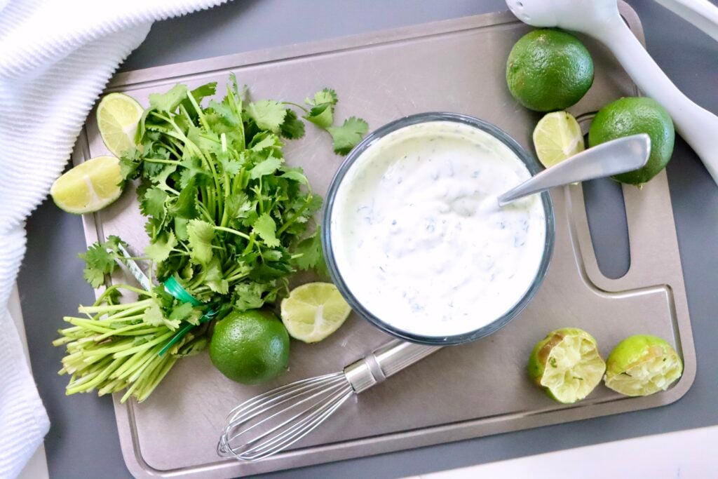 Creamy cilantro lime crema made with Greek yogurt served in a white bowl with a spoon, perfect healthy sauce for tacos and bowls.