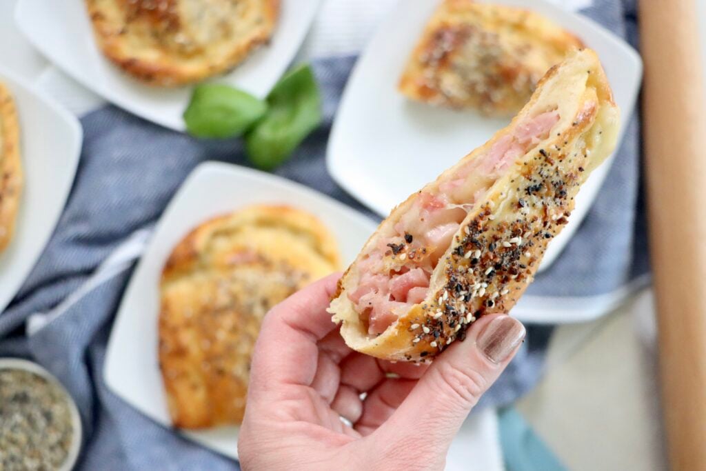 Freshly baked ham and cheese hot pockets cut open showing gooey melted cheddar and diced Canadian bacon filling.
