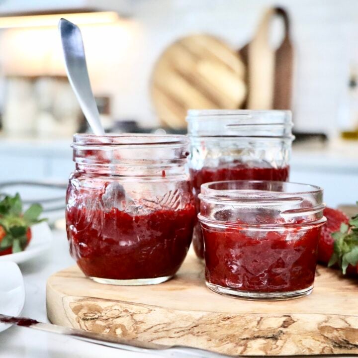 Low sugar homemade strawberry jam in a glass jar with fresh strawberries on the side