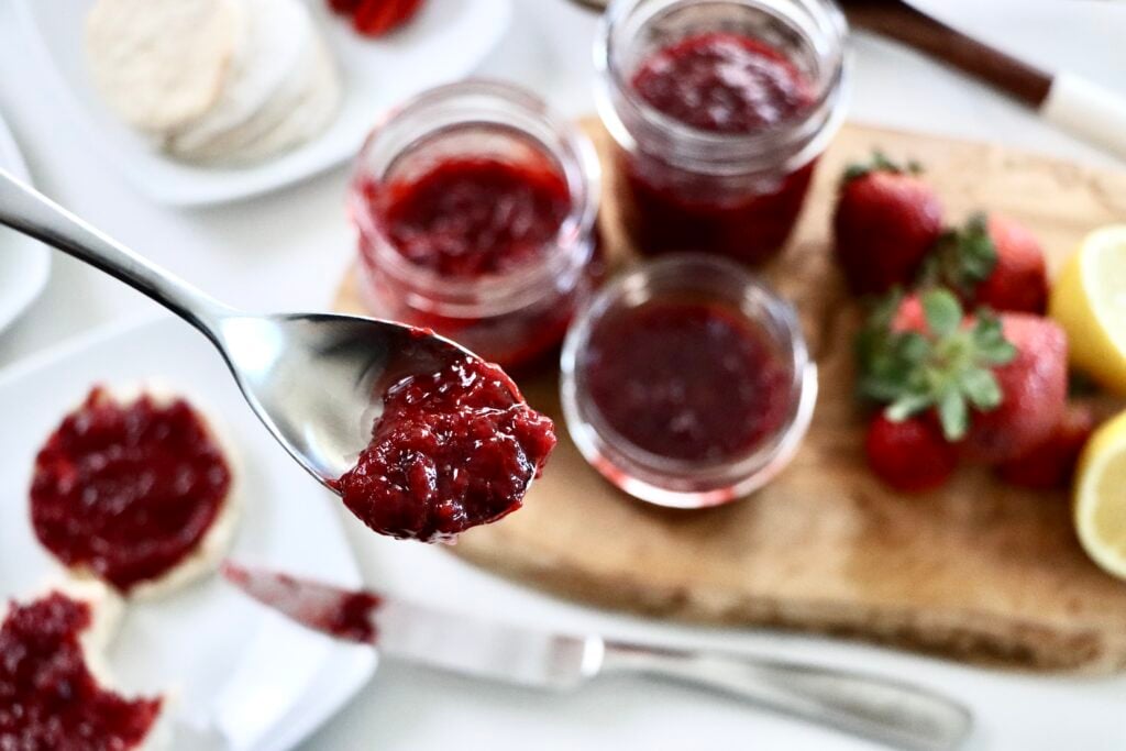 Fresh strawberry jam in a jar with a spoon showing smooth, spreadable consistency